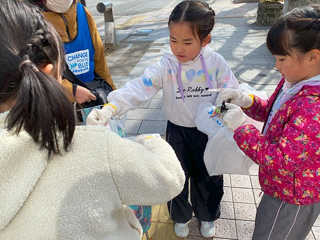 ごみを分別する女の子3人とそれを見つめる女性