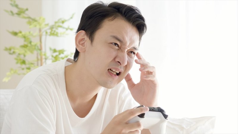 ゲームコントローラーを持って顔をしかめる男性
