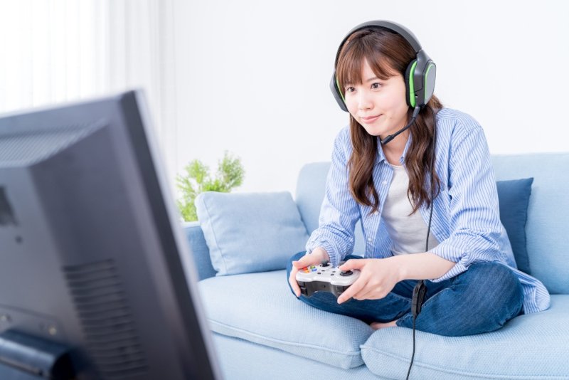 ヘッドホンをしてゲームコントローラーを持った女性がゲームをプレイする様子