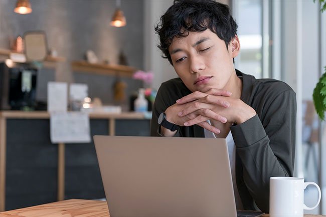 ノートパソコンの前で困った表情をする男性