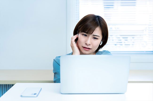 イヤホンをおさえてノートパソコンを見ながら困っている女性