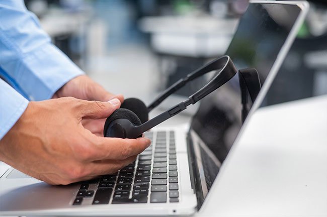 ノートパソコンンの上でヘッドホンを持つ手のイメージ